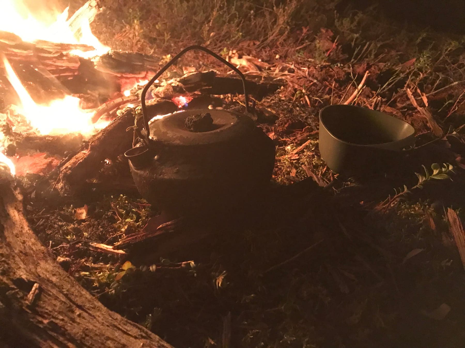 Sotig kaffepanna och kåsa intill lägerelden i mörkret