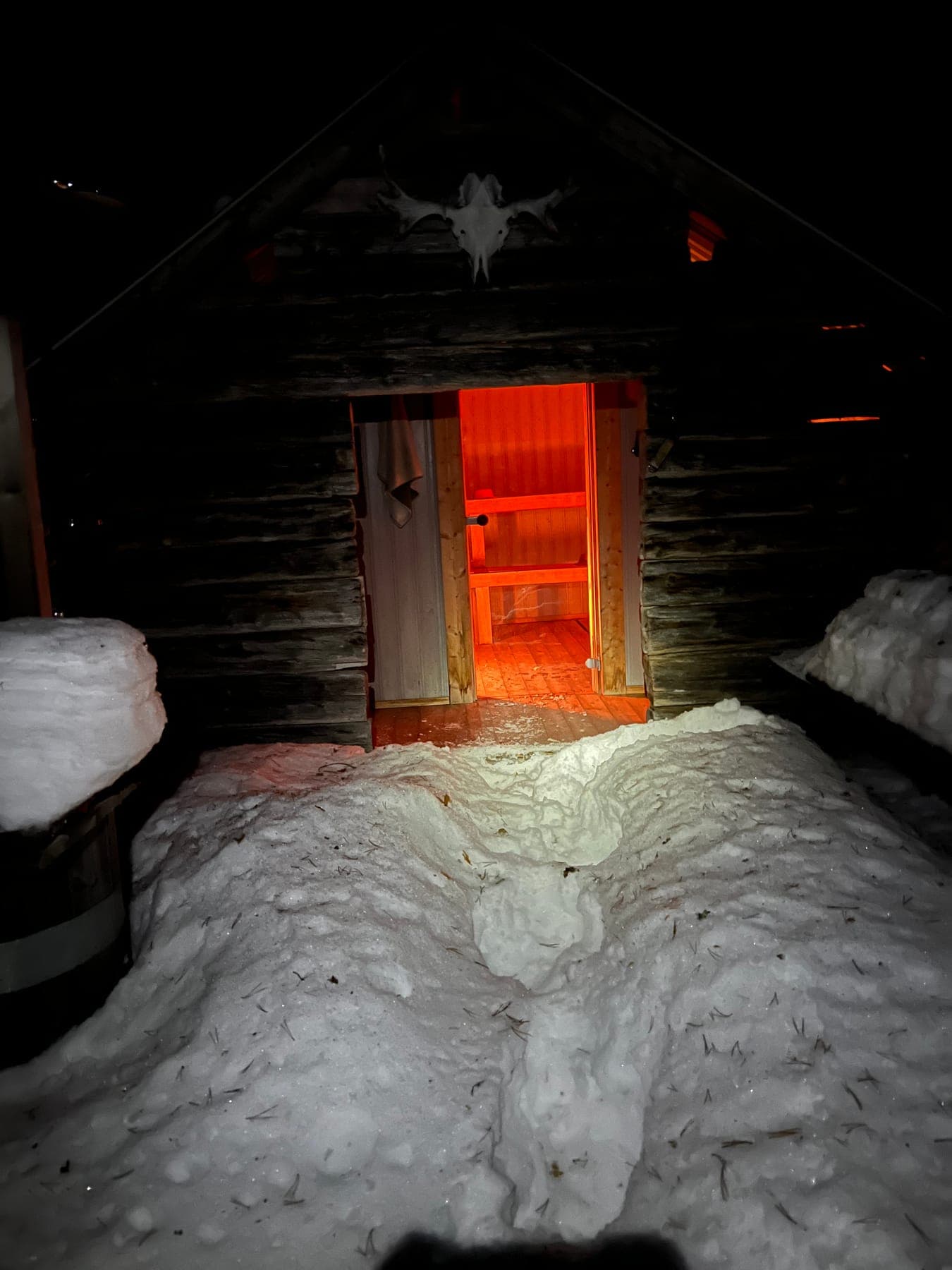 Timrad bastu i vintermörker med varmt ljus ur den öppna dörren och stig i djup snö