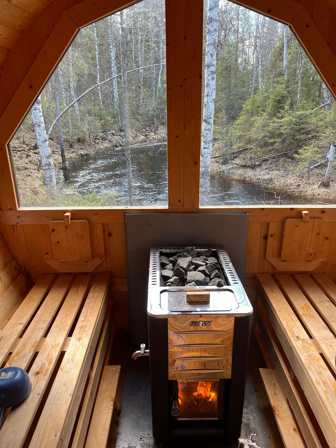Bastuns interiör med vedeldad kamin och stort fönster mot ån Krikijoki