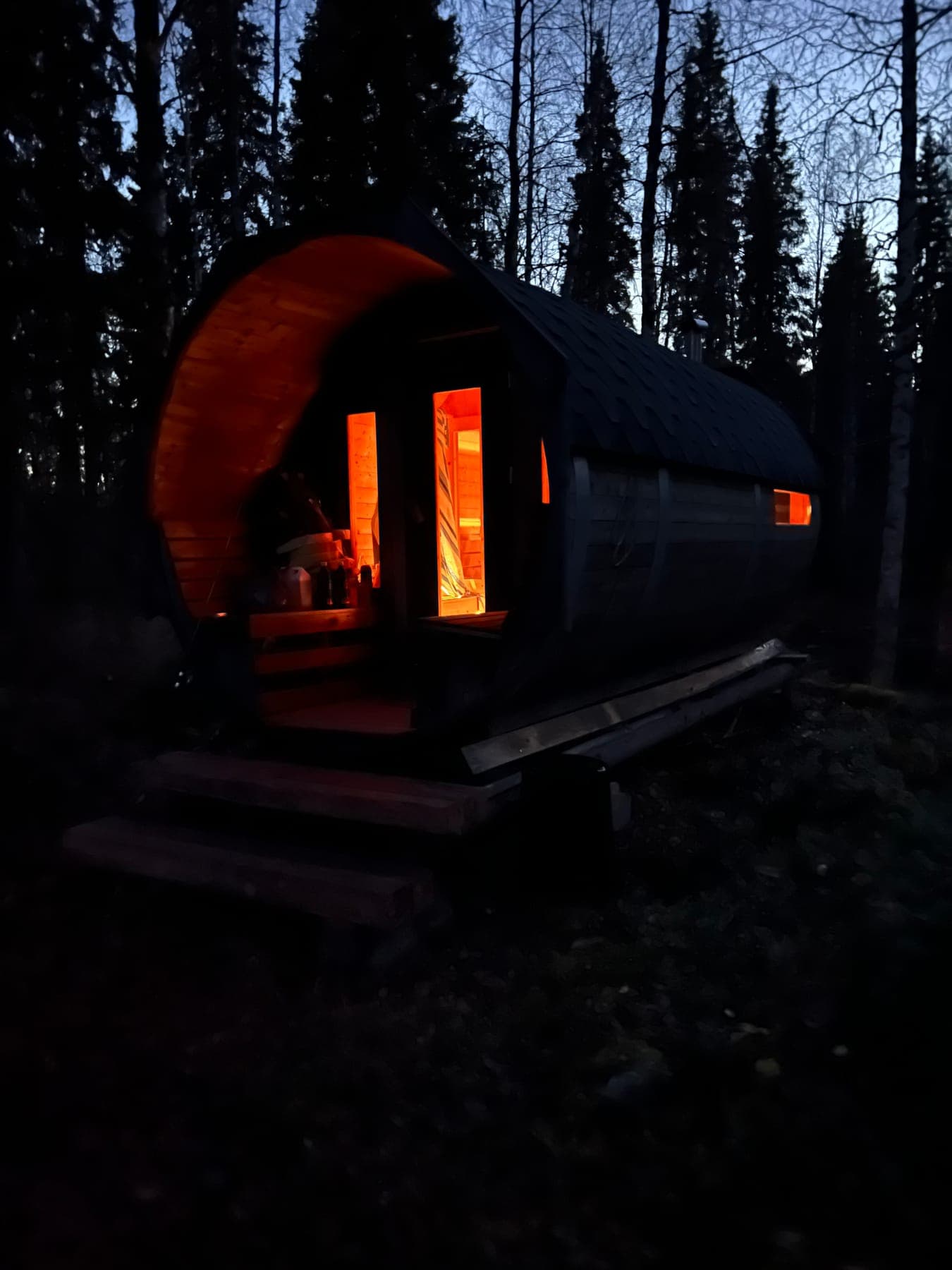 Bastun i skymning med varmt ljus i dörr och fönster, ån intill